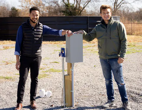 Two men beside a utility pedestal on a gravel RV site