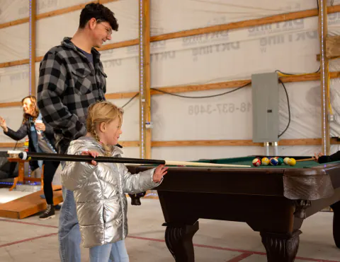 Girl lining up a billiards shot with her family