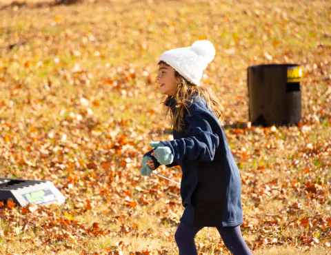 Girl in a white knit hat running through autumn leaves