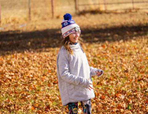 Girl in a knit hat standing in autumn leaves
