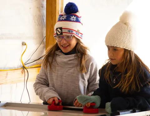 Two girls playing air hockey in the game room at Lake Hudson Resort