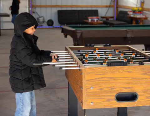 Boy in a black coat playing foosball near the billiards table