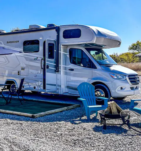 Motorhome on a gravel RV site with Adirondack chairs and a fire pit